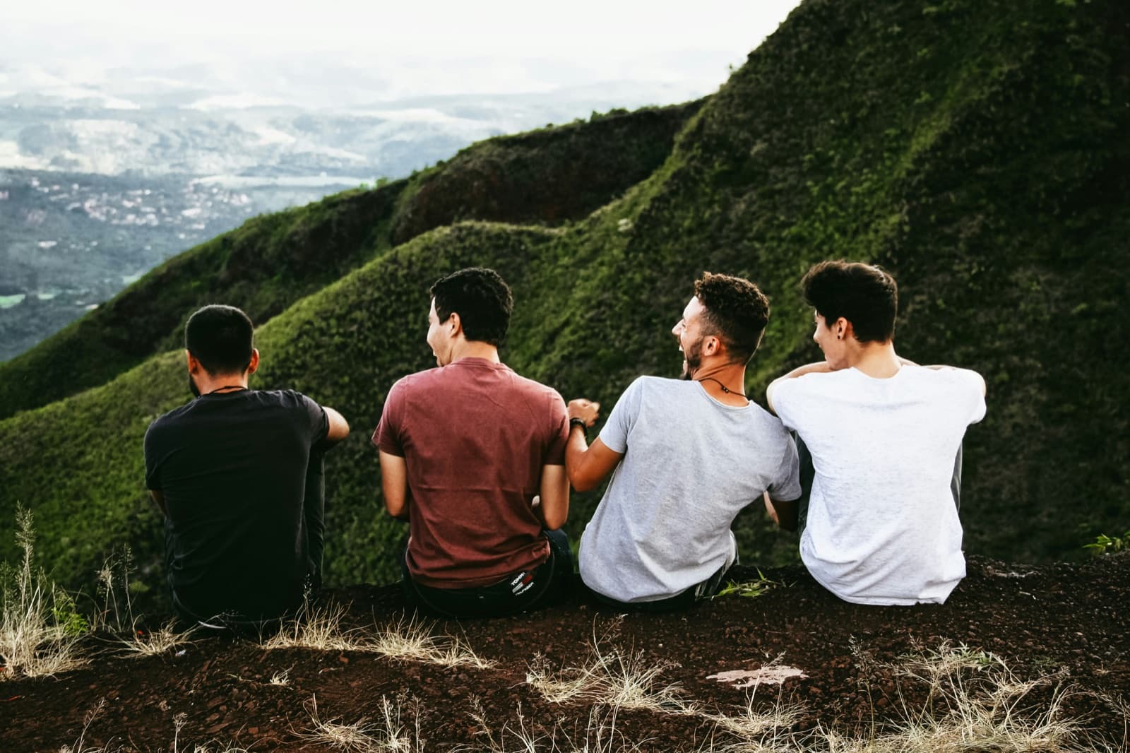Four friends sitting together on a hilltop, looking out over a green valley